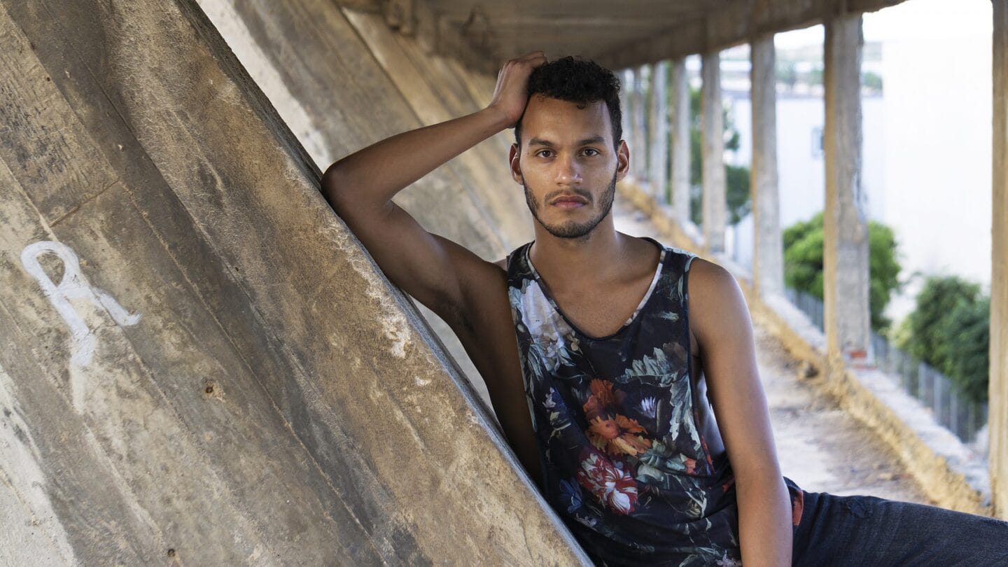 Hombre joven apoyado en muro de hormigón bajo puente