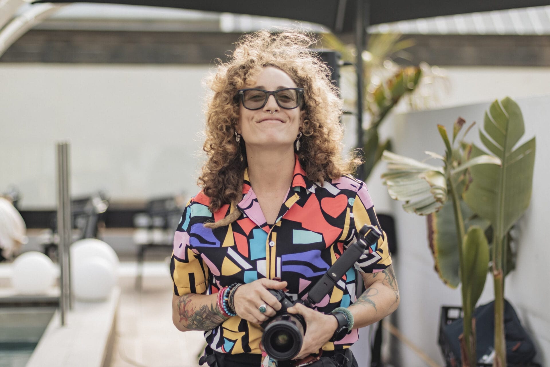 Mujer con pelo rizado y gafas sosteniendo cámara profesional
