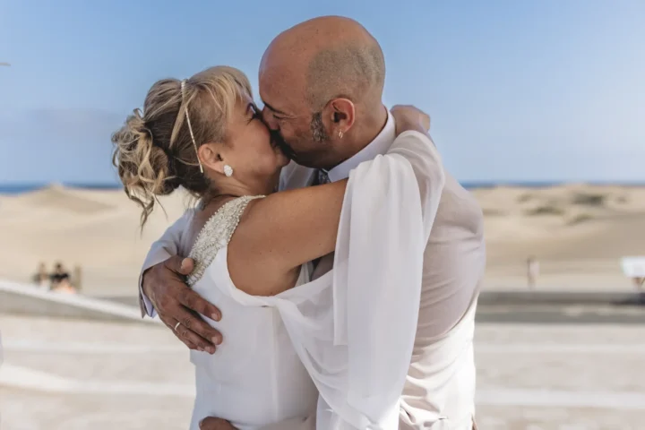 Pareja besándose en la playa con traje blanco